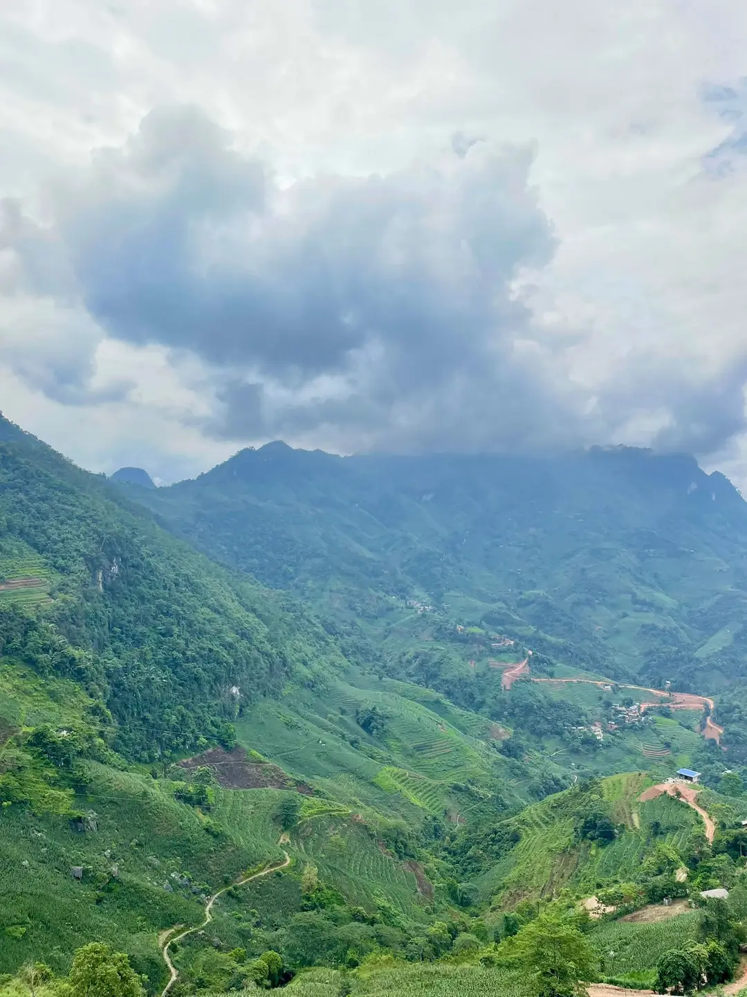 Un panorama grandiose sur de hautes montagnes verdoyantes et des vallées cultivées sous un ciel chargé de gros nuages blancs et gris au Vietnam.