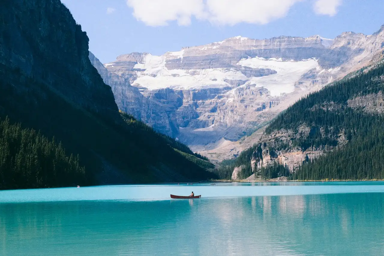 Eaux turquoise du lac Louise bordées de falaises boisées avec le glacier Victoria en arrière-plan dans les Rocheuses canadiennes