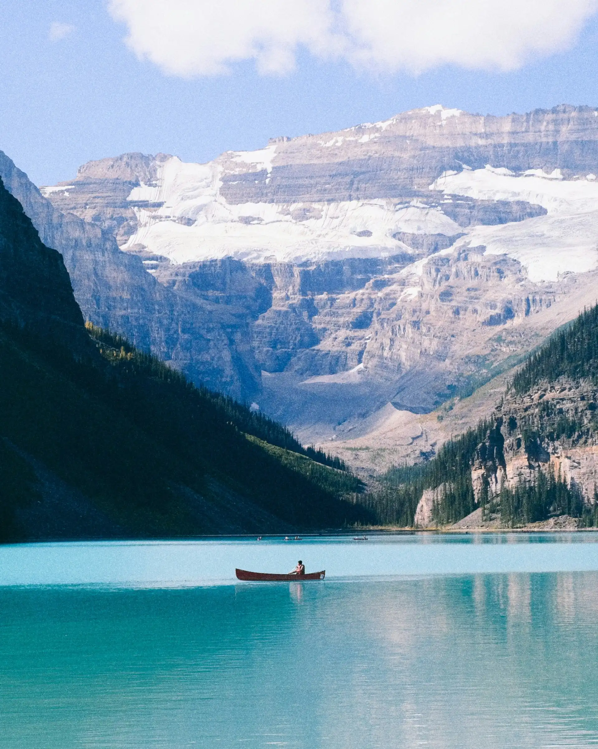 Eaux turquoise du lac Louise bordées de falaises boisées avec le glacier Victoria en arrière-plan dans les Rocheuses canadiennes