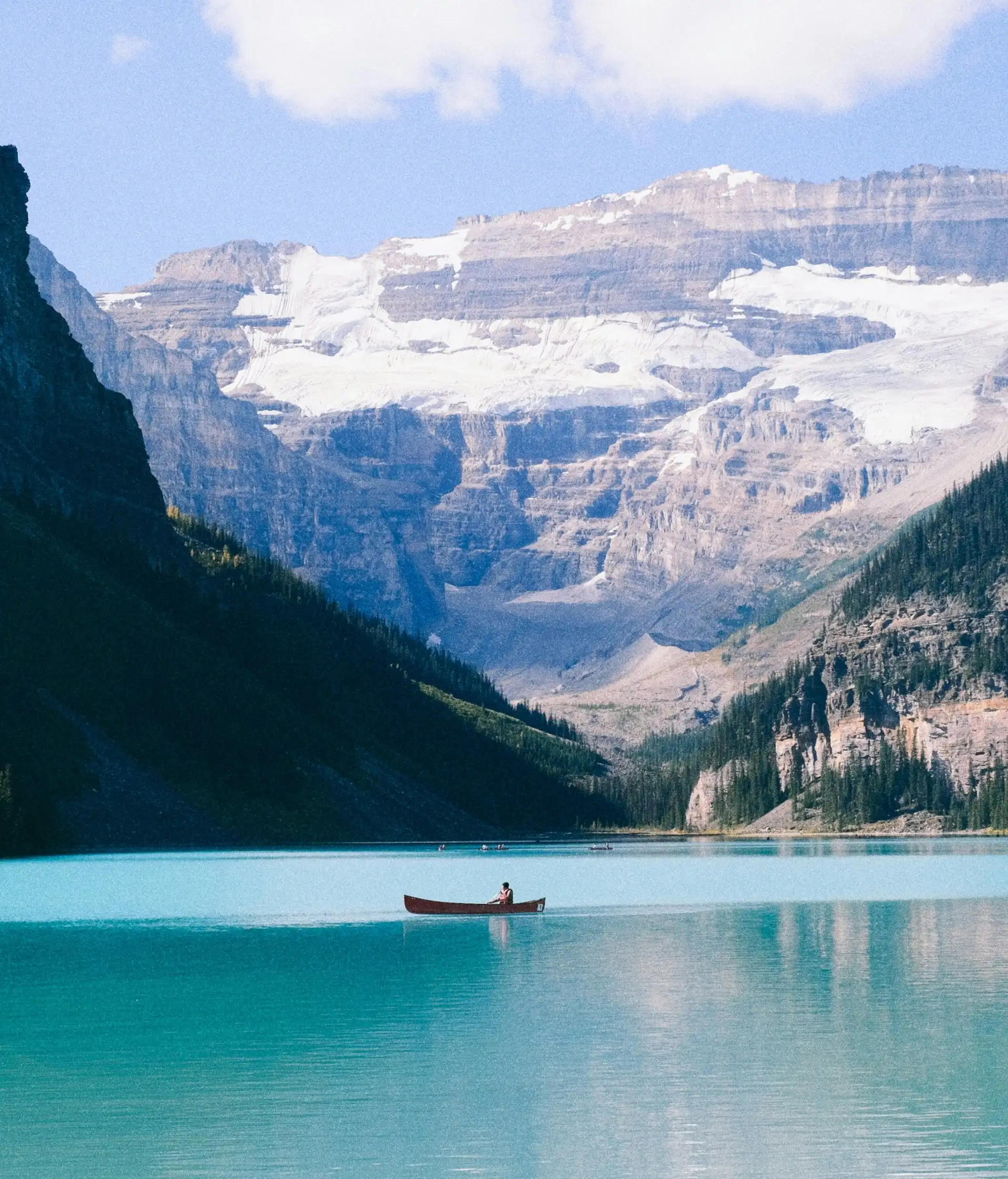 Eaux turquoise du lac Louise bordées de falaises boisées avec le glacier Victoria en arrière-plan dans les Rocheuses canadiennes