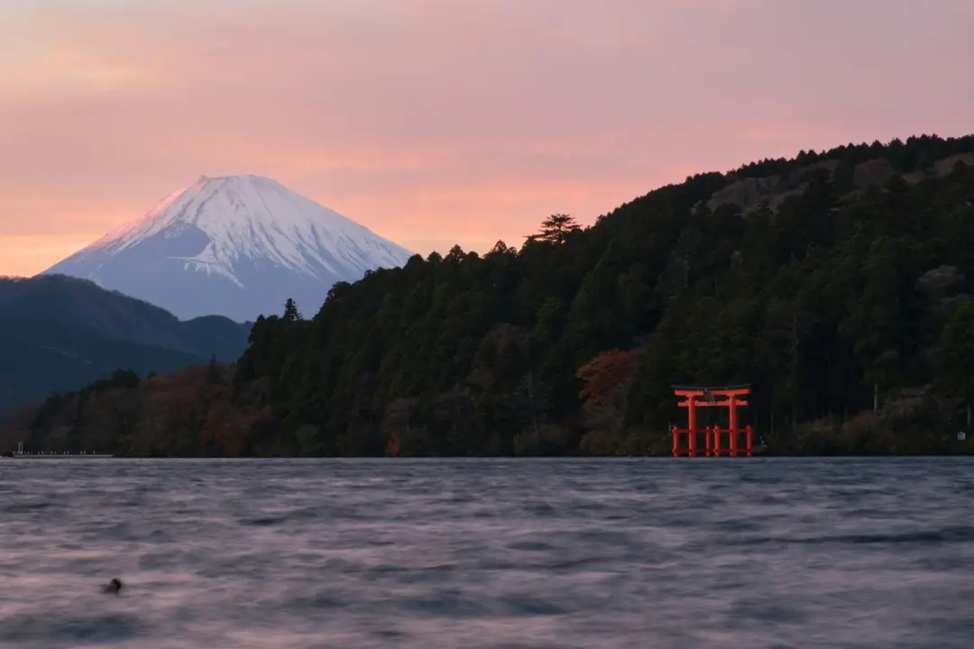 Le grand torii vermillon du sanctuaire de Hakone dressé dans l'eau du lac Ashi, avec le mont Fuji enneigé au loin en arrière-plan.
