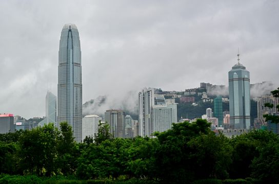 Vue sur les gratte-ciel du quartier de Central à Hong Kong depuis Victoria Harbour, avec le Two International Finance Centre et des collines verdoyantes sous la brume.