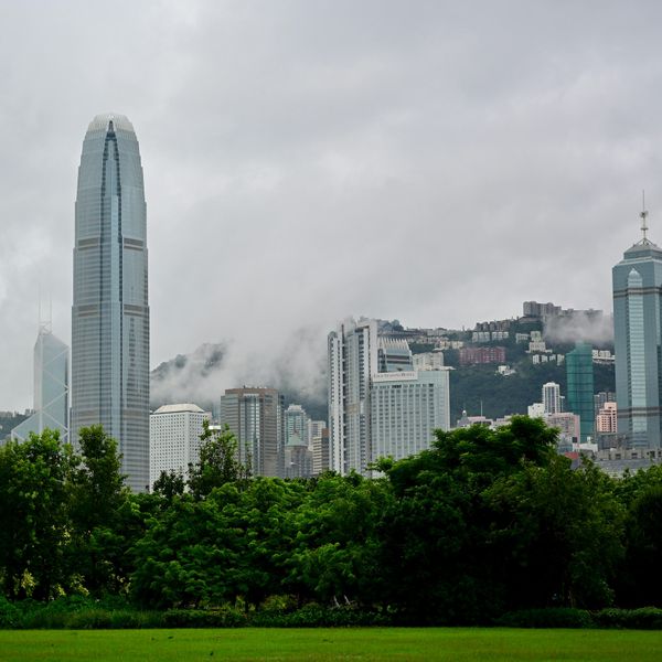 Vue sur les gratte-ciel du quartier de Central à Hong Kong depuis Victoria Harbour, avec le Two International Finance Centre et des collines verdoyantes sous la brume.