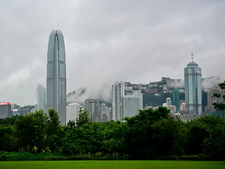 Vue sur les gratte-ciel du quartier de Central à Hong Kong depuis Victoria Harbour, avec le Two International Finance Centre et des collines verdoyantes sous la brume.