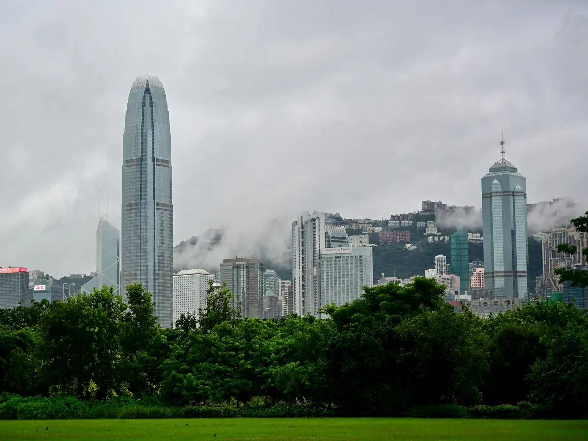 Vue sur les gratte-ciel du quartier de Central à Hong Kong depuis Victoria Harbour, avec le Two International Finance Centre et des collines verdoyantes sous la brume.