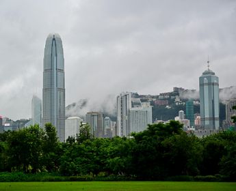 Vue sur les gratte-ciel du quartier de Central à Hong Kong depuis Victoria Harbour, avec le Two International Finance Centre et des collines verdoyantes sous la brume.
