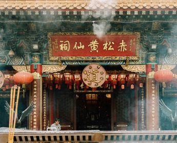 Entrée ornée du temple taoïste Wong Tai Sin à Kowloon, montrant des lanternes rouges, des inscriptions calligraphiées et de la fumée d'encens rituelle.
