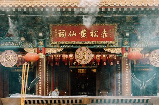 Entrée ornée du temple taoïste Wong Tai Sin à Kowloon, montrant des lanternes rouges, des inscriptions calligraphiées et de la fumée d'encens rituelle.