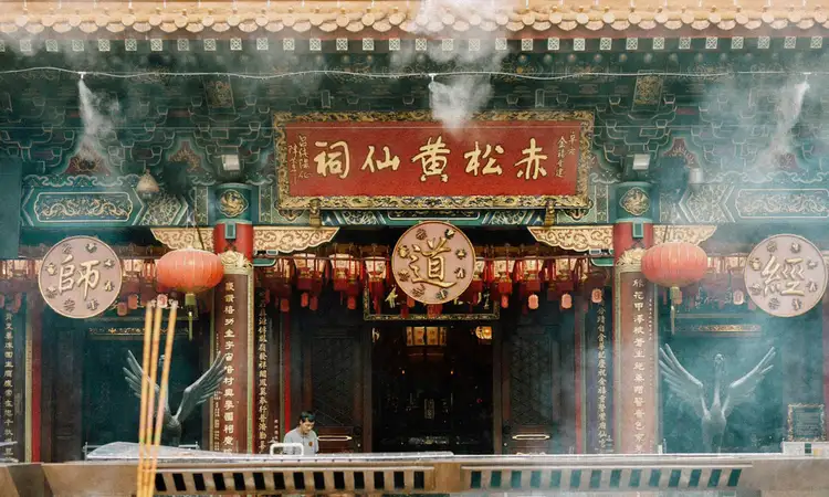 Entrée ornée du temple taoïste Wong Tai Sin à Kowloon, montrant des lanternes rouges, des inscriptions calligraphiées et de la fumée d'encens rituelle.