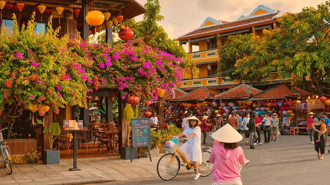 Voyage en Asie – Une femme à vélo dans les rues du centre historique de Hoi An au Vietnam, bordées de bougainvilliers et de lanternes.