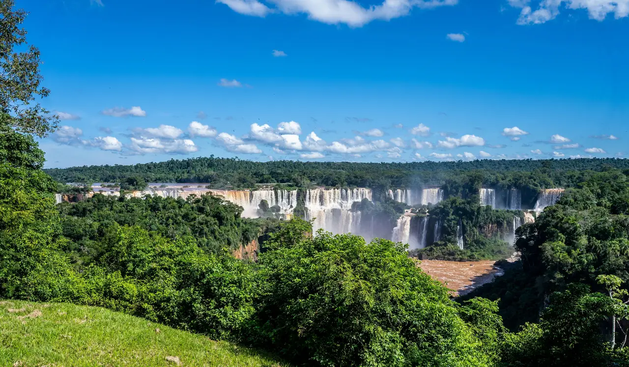 Voyage au Brésil – Vue panoramique spectaculaire sur l'immense front des chutes d'Iguaçu entourées par la forêt tropicale sous un ciel bleu.