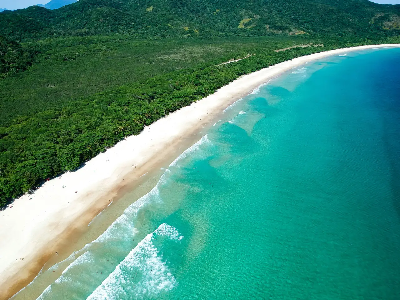 Voyage au Brésil – Vue aérienne panoramique de la plage sauvage de Lopes Mendes à Ilha Grande, sa longue étendue de sable blanc et ses eaux turquoise bordées par la forêt tropicale.