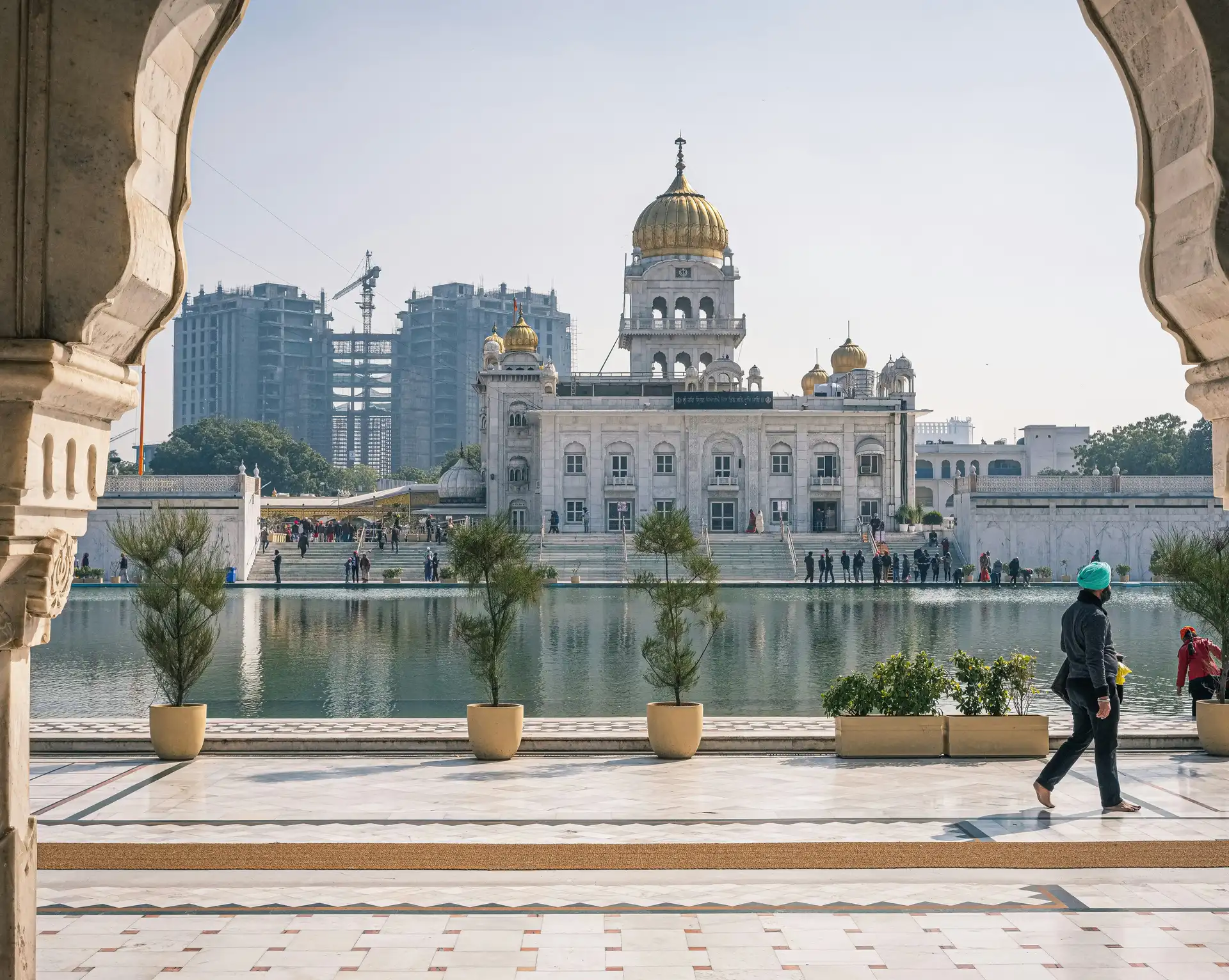 Vue cadrée par une arche en pierre du temple sikh Gurudwara Bangla Sahib et son bassin à New Delhi[cite: 10].