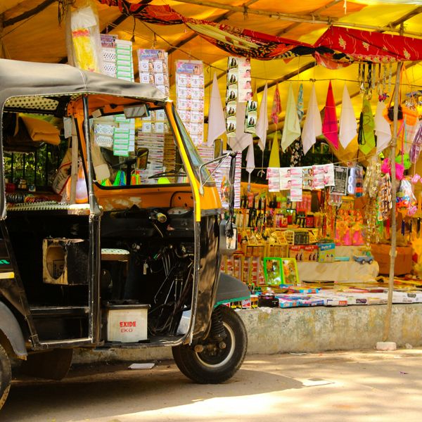 Un rickshaw noir et jaune stationné devant une échoppe de rue colorée vendant des articles d'artisanat et des souvenirs sous un auvent jaune à Mumbai.