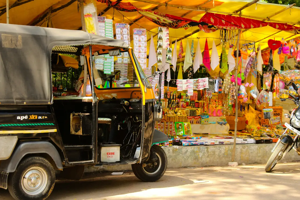 Un rickshaw noir et jaune stationné devant une échoppe de rue colorée vendant des articles d'artisanat et des souvenirs sous un auvent jaune à Mumbai.