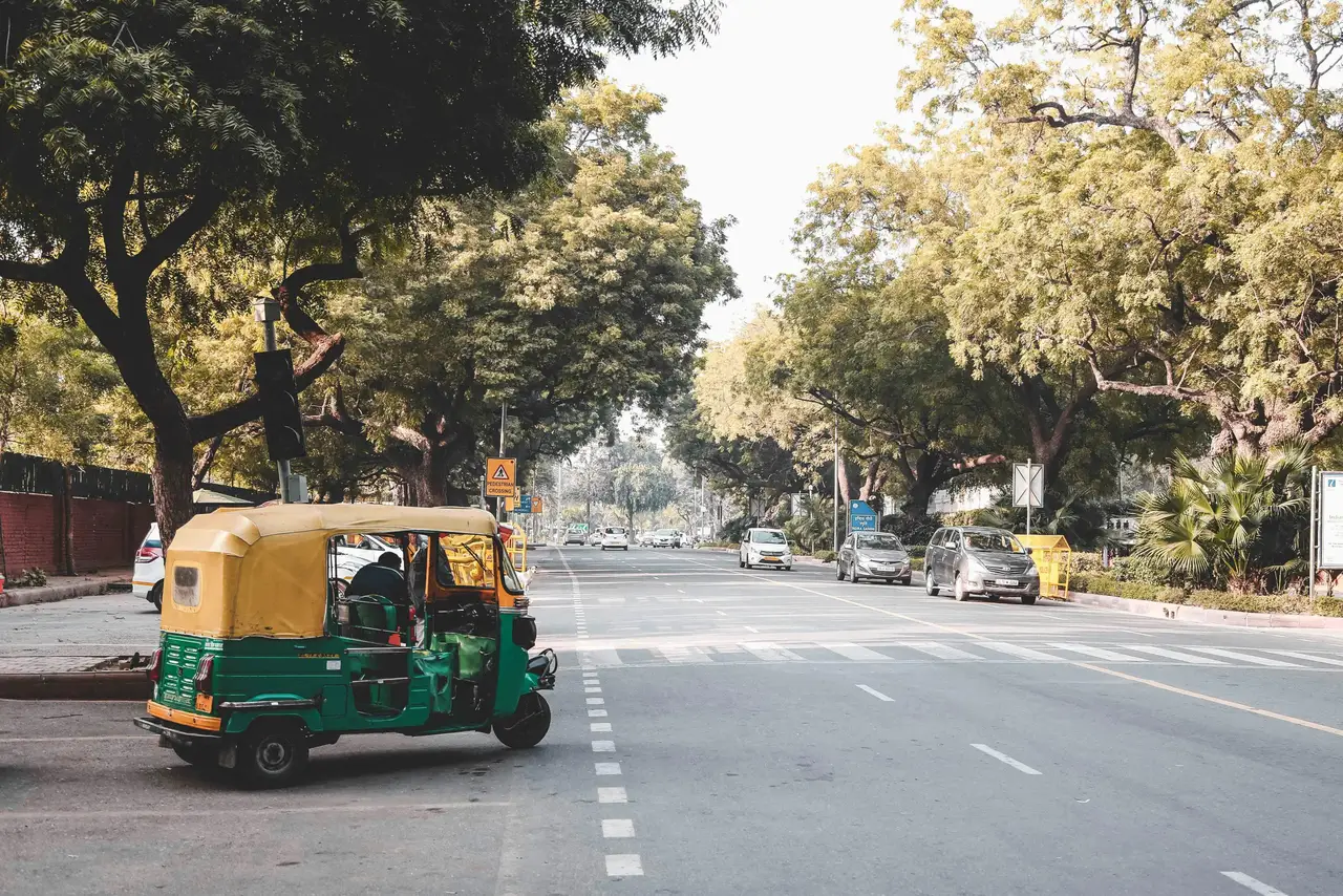 Un rickshaw vert et jaune stationné sur une large avenue arborée de Delhi lors d'une journée ensoleillée en Inde.