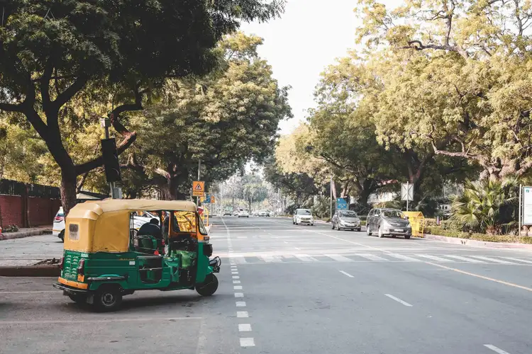 Un rickshaw vert et jaune stationné sur une large avenue arborée de Delhi lors d'une journée ensoleillée en Inde.