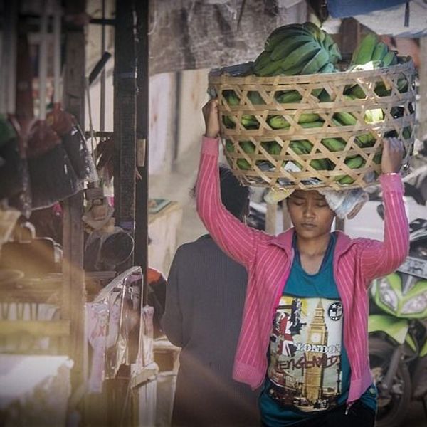 Voyage en Asie — Femme balinaise portant un panier de fruits au marché : scène de vie quotidienne et travail acharné.