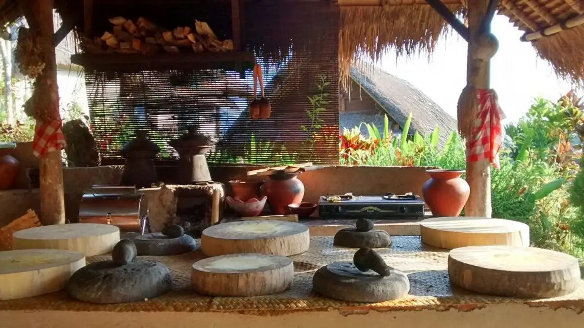 Une cuisine balinaise traditionnelle en plein air sous un toit de chaume, aménagée avec des ustensiles en pierre et des ingrédients locaux pour un atelier culinaire à Sidemen.