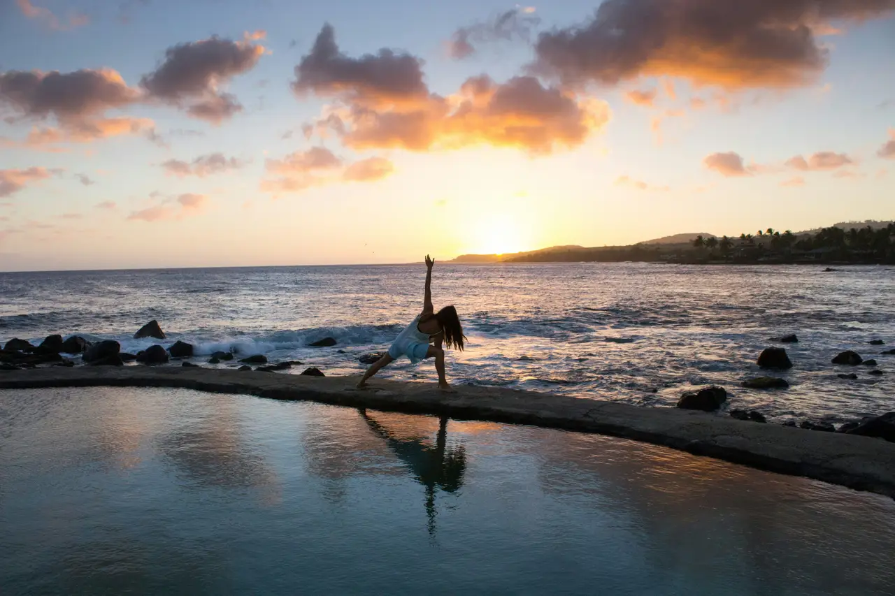 Une personne en silhouette pratiquant une posture de yoga au bord d'une piscine face à l'océan, sous les lueurs dorées d'un coucher de soleil à Bali.