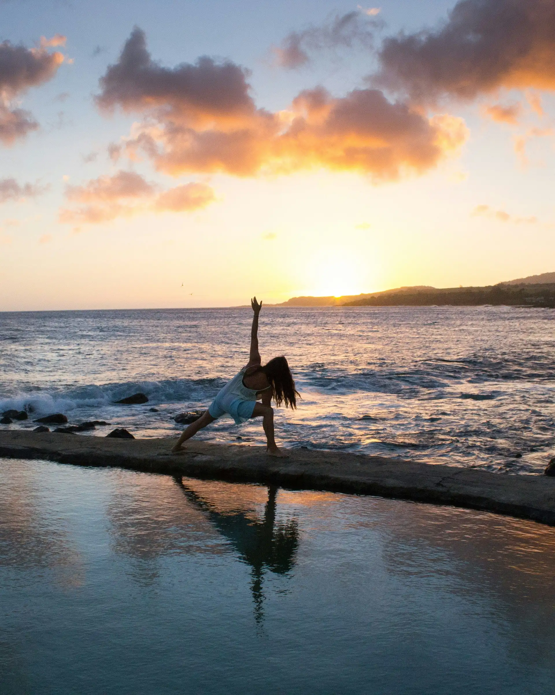 Une personne en silhouette pratiquant une posture de yoga au bord d'une piscine face à l'océan, sous les lueurs dorées d'un coucher de soleil à Bali.