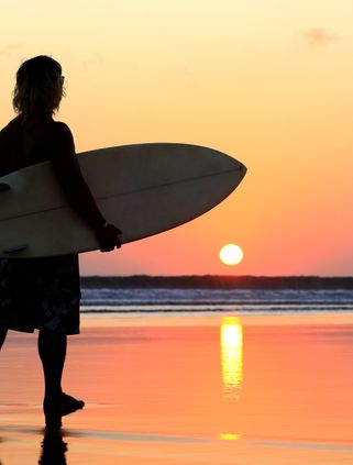 Voyage en Asie — Surfeur au coucher du soleil sur une plage de Bali, idéal pour un voyage d'été et d'aventure — Shanti Travel