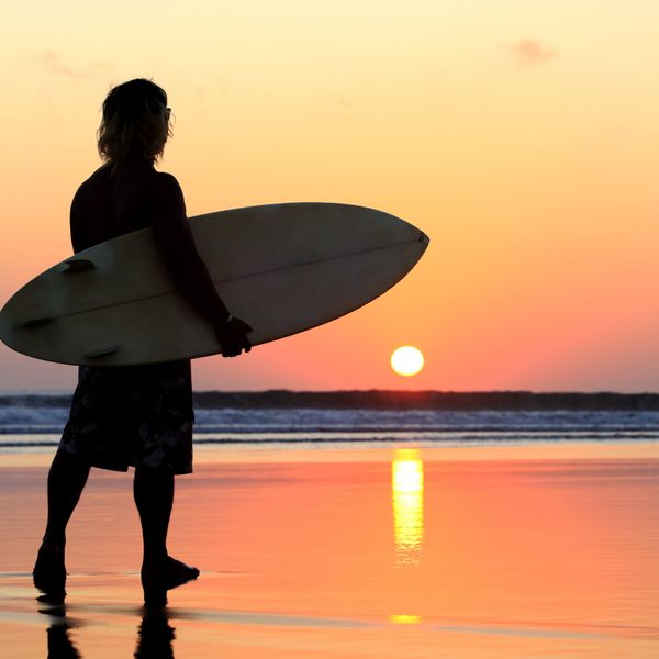 Voyage en Asie — Surfeur au coucher du soleil sur une plage de Bali, idéal pour un voyage d'été et d'aventure — Shanti Travel