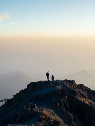 Travel in Asia - Two hikers stand on the summit of Mount Rinjani surrounded by a sea of clouds in Lombok, Indonesia