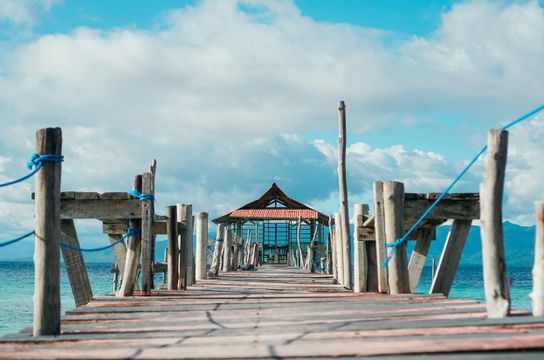 Voyage en Asie — pont en bois menant à un petit abri au bord de la mer aux Moluques en Indonésie, une expérience authentique guidée par notre expertise locale — Shanti Travel