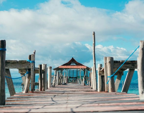 Voyage en Asie — pont en bois menant à un petit abri au bord de la mer aux Moluques en Indonésie, une expérience authentique guidée par notre expertise locale — Shanti Travel