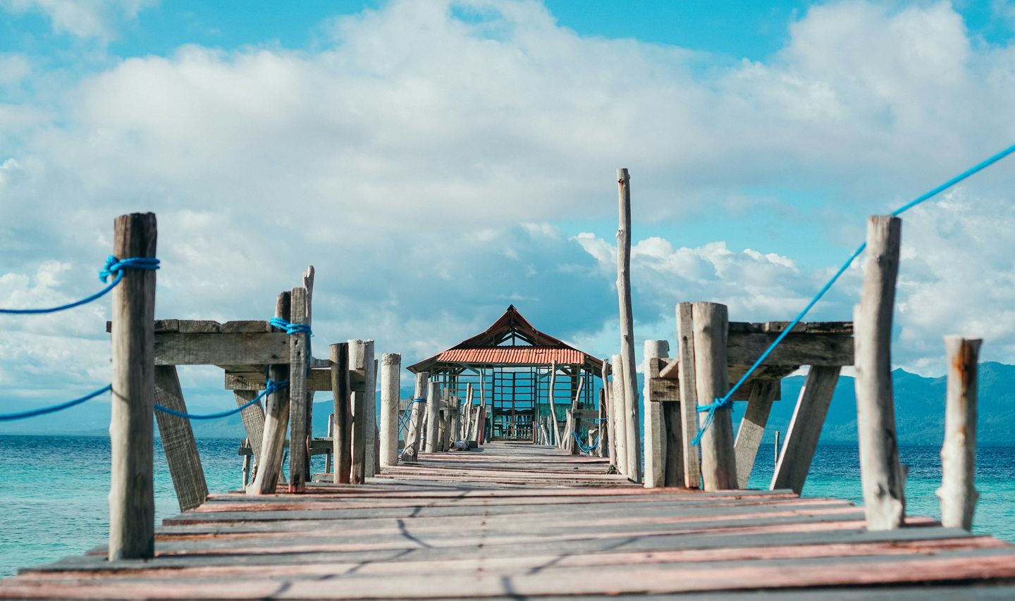 Voyage en Asie — pont en bois menant à un petit abri au bord de la mer aux Moluques en Indonésie, une expérience authentique guidée par notre expertise locale — Shanti Travel