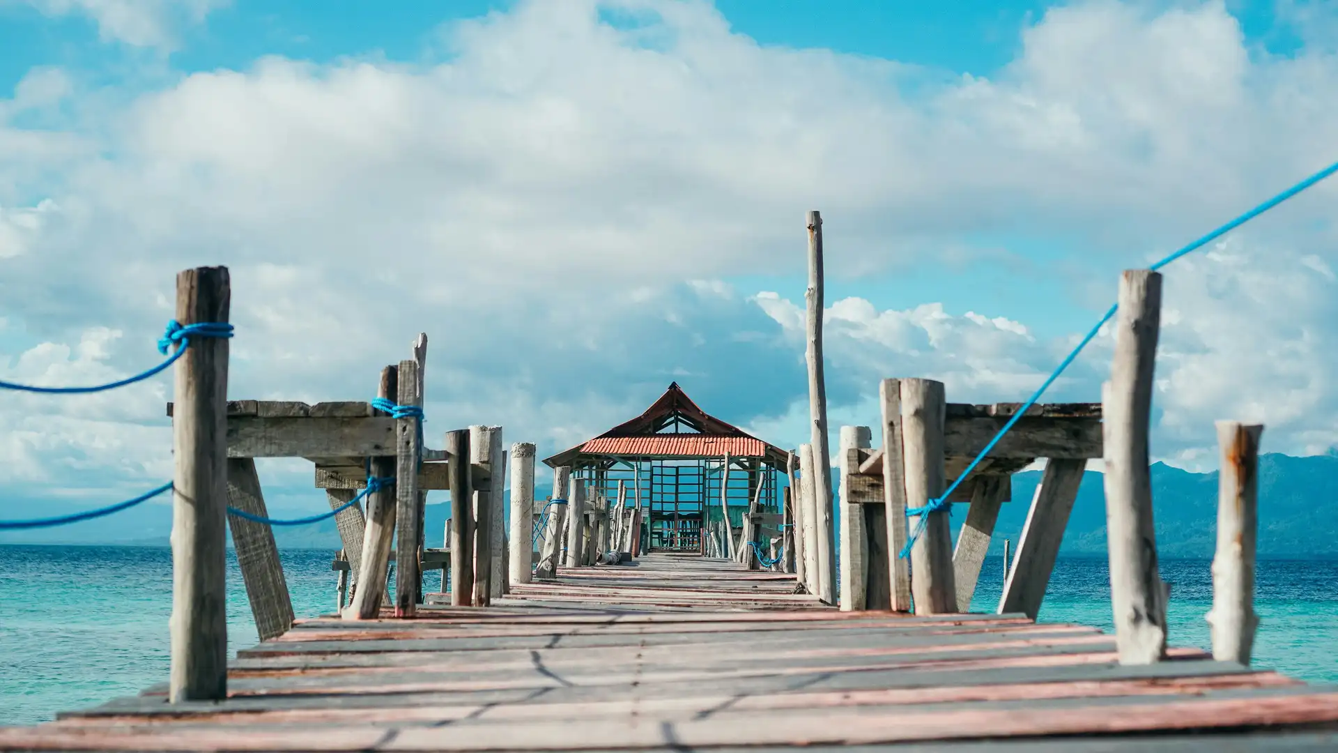Voyage en Asie — pont en bois menant à un petit abri au bord de la mer aux Moluques en Indonésie, une expérience authentique guidée par notre expertise locale — Shanti Travel