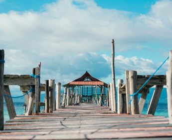 Voyage en Asie — pont en bois menant à un petit abri au bord de la mer aux Moluques en Indonésie, une expérience authentique guidée par notre expertise locale — Shanti Travel