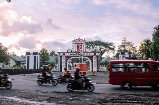 Voyage en Asie — scène urbaine animée à Ambon avec motos et minibus devant la porte emblématique de la ville, témoignage authentique de la vie locale grâce à notre expertise — Shanti Travel
