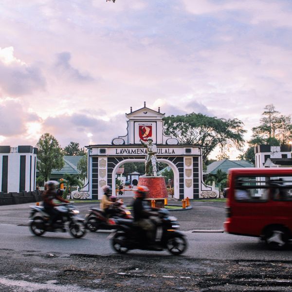 Voyage en Asie — scène urbaine animée à Ambon avec motos et minibus devant la porte emblématique de la ville, témoignage authentique de la vie locale grâce à notre expertise — Shanti Travel