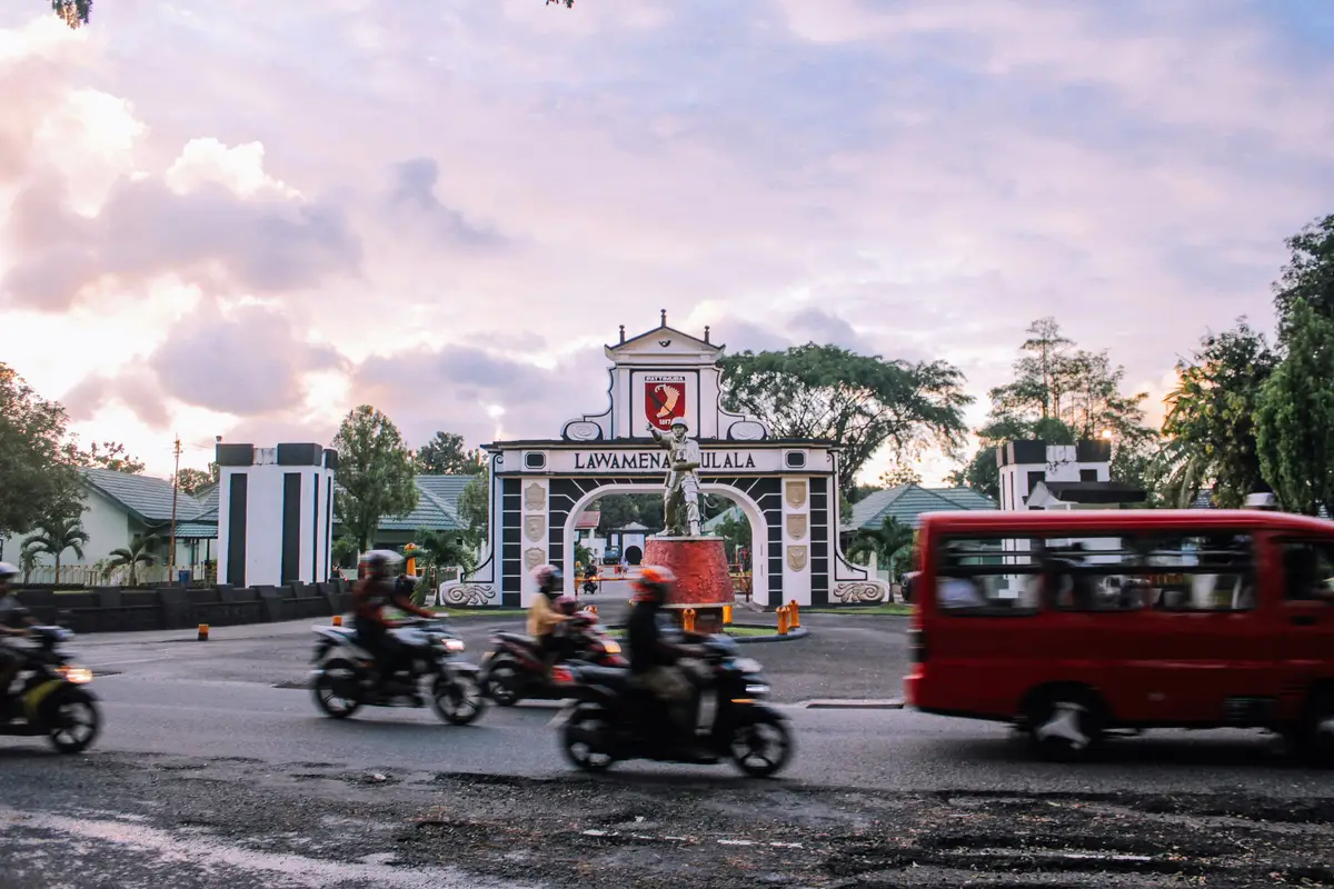 Voyage en Asie — scène urbaine animée à Ambon avec motos et minibus devant la porte emblématique de la ville, témoignage authentique de la vie locale grâce à notre expertise — Shanti Travel