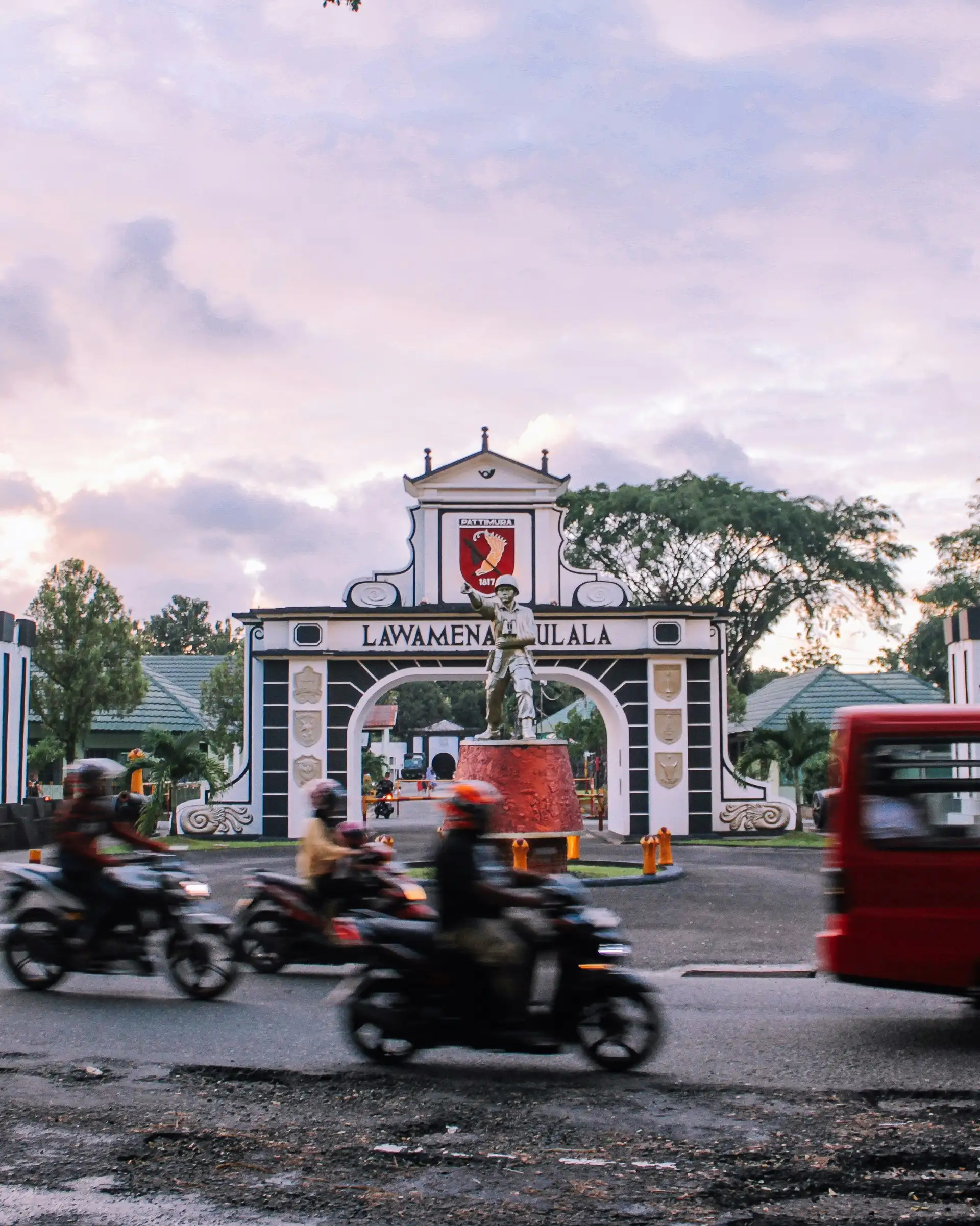 Voyage en Asie — scène urbaine animée à Ambon avec motos et minibus devant la porte emblématique de la ville, témoignage authentique de la vie locale grâce à notre expertise — Shanti Travel
