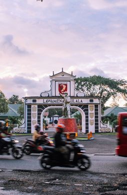 Voyage en Asie — scène urbaine animée à Ambon avec motos et minibus devant la porte emblématique de la ville, témoignage authentique de la vie locale grâce à notre expertise — Shanti Travel