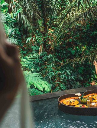 Travel in Asia - A woman with arms raised in happiness in a pool about to enjoy a floating breakfast served on a heart-shaped tray at a resort in Bali