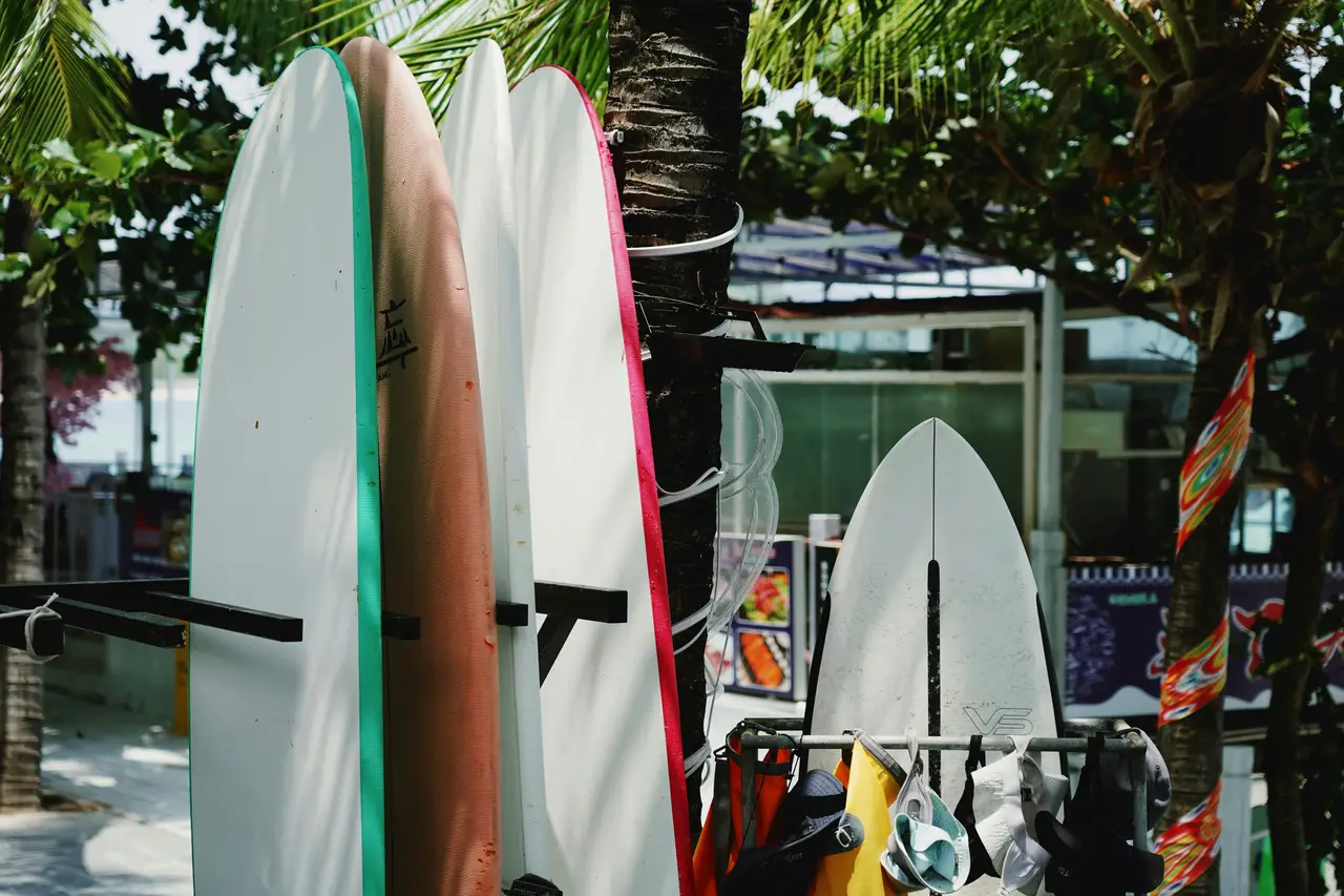 Plusieurs planches de surf colorées rangées verticalement à l'ombre de palmiers tropicaux à Cocoa Beach