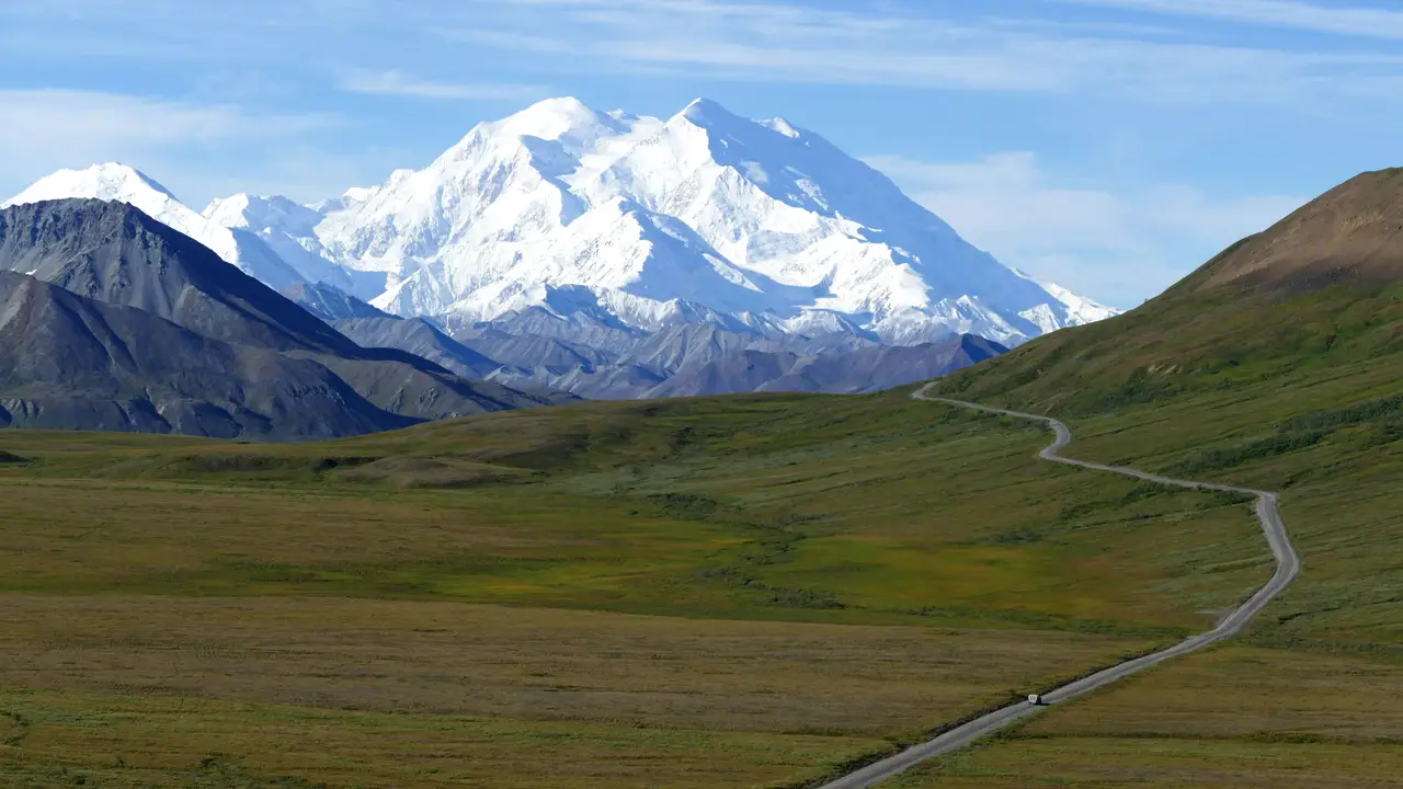 Route sinueuse traversant la toundra verdoyante menant vers le sommet enneigé du mont Denali sous un ciel bleu dégagé
