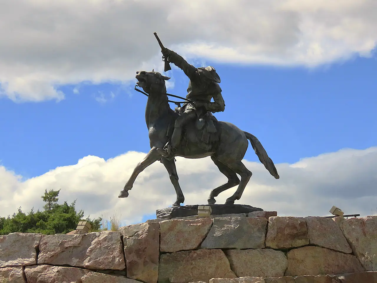 Statue équestre en bronze de Buffalo Bill chevauchant et levant son fusil sous un ciel bleu nuageux à Cody dans le Wyoming