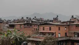 Toits et façades en brique rouge de maisons traditionnelles népalaises dans la vallée de Katmandou avec les collines en arrière-plan.