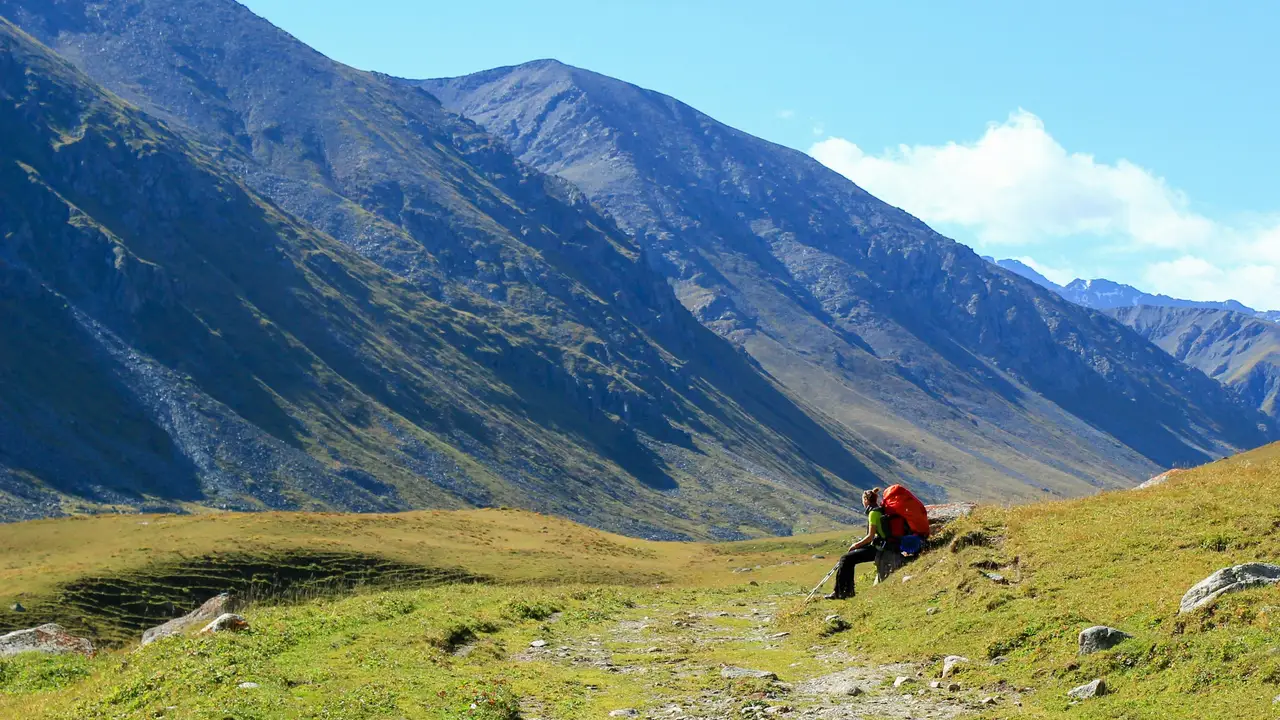 Voyage au Kirghizistan - Randonneuse faisant une pause assise face aux montagnes
