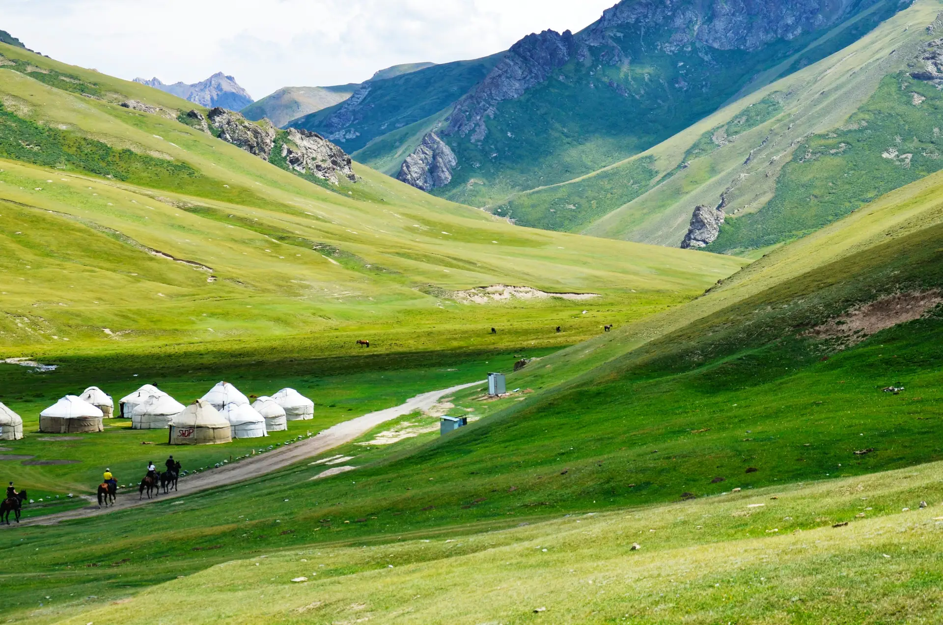 Voyage au Kirghizistan — Yourtes blanches et cavaliers dans une vallée verdoyante au pied des montagnes Tian Shan.
