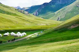 Voyage au Kirghizistan — Yourtes blanches et cavaliers dans une vallée verdoyante au pied des montagnes Tian Shan.
