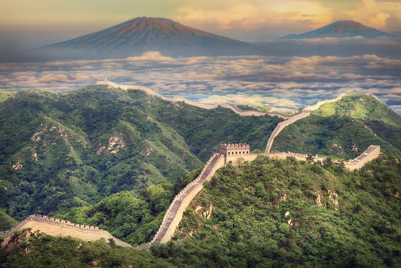Vue panoramique de la Grande Muraille de Chine serpentant sur des crêtes de montagnes verdoyantes sous une lumière de fin de journée.