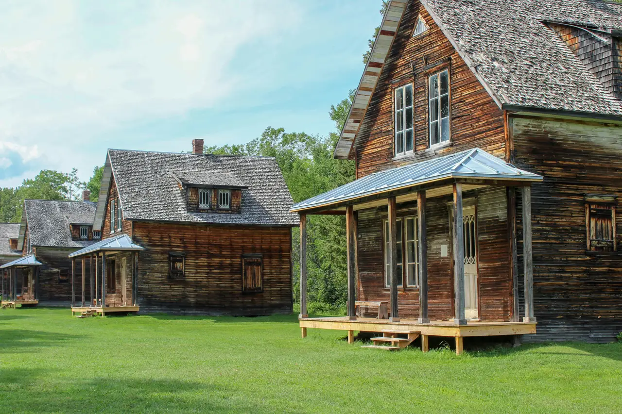 Maisons traditionnelles en bois d'époque bordant une allée d'herbe verte sous un ciel bleu au village historique de Val-Jalbert près du lac Saint-Jean