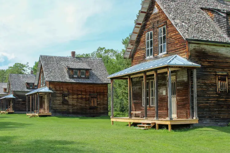 Maisons traditionnelles en bois d'époque bordant une allée d'herbe verte sous un ciel bleu au village historique de Val-Jalbert près du lac Saint-Jean