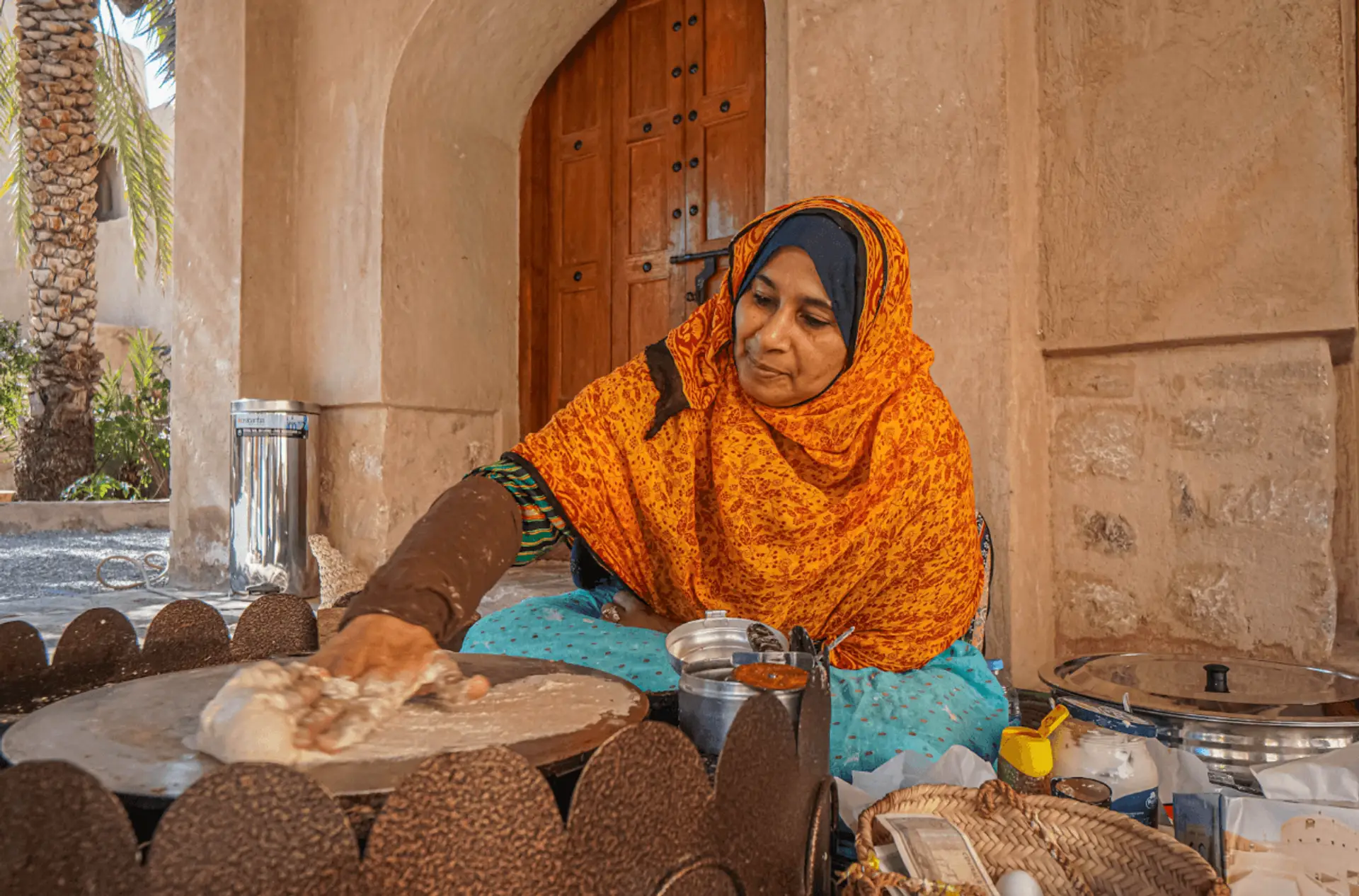 Femme omanaise vêtue d'un voile orange préparant du pain traditionnel sur une plaque de cuisson circulaire.